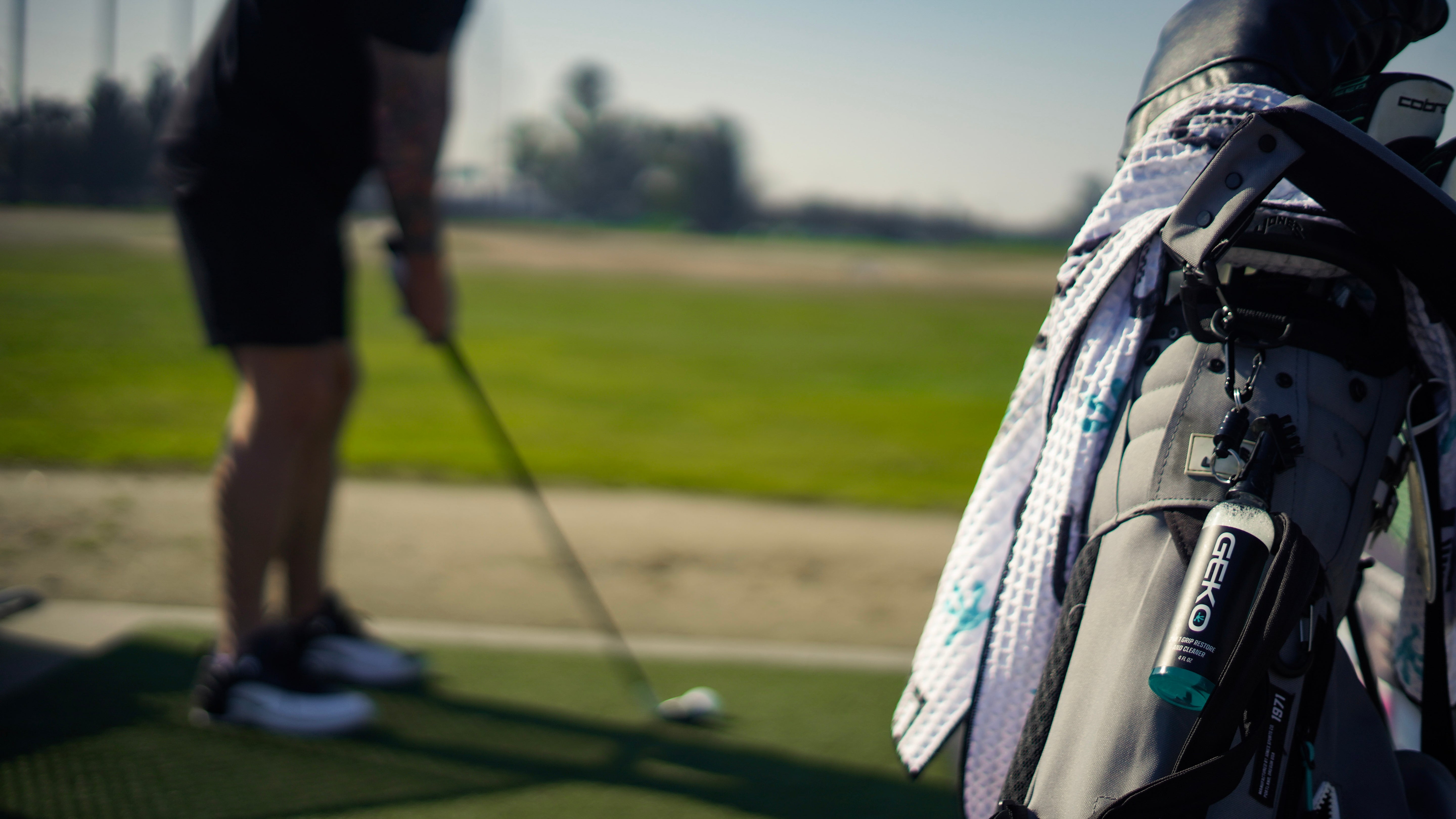 Golfer practicing on a driving range with a golf bag in the foreground.