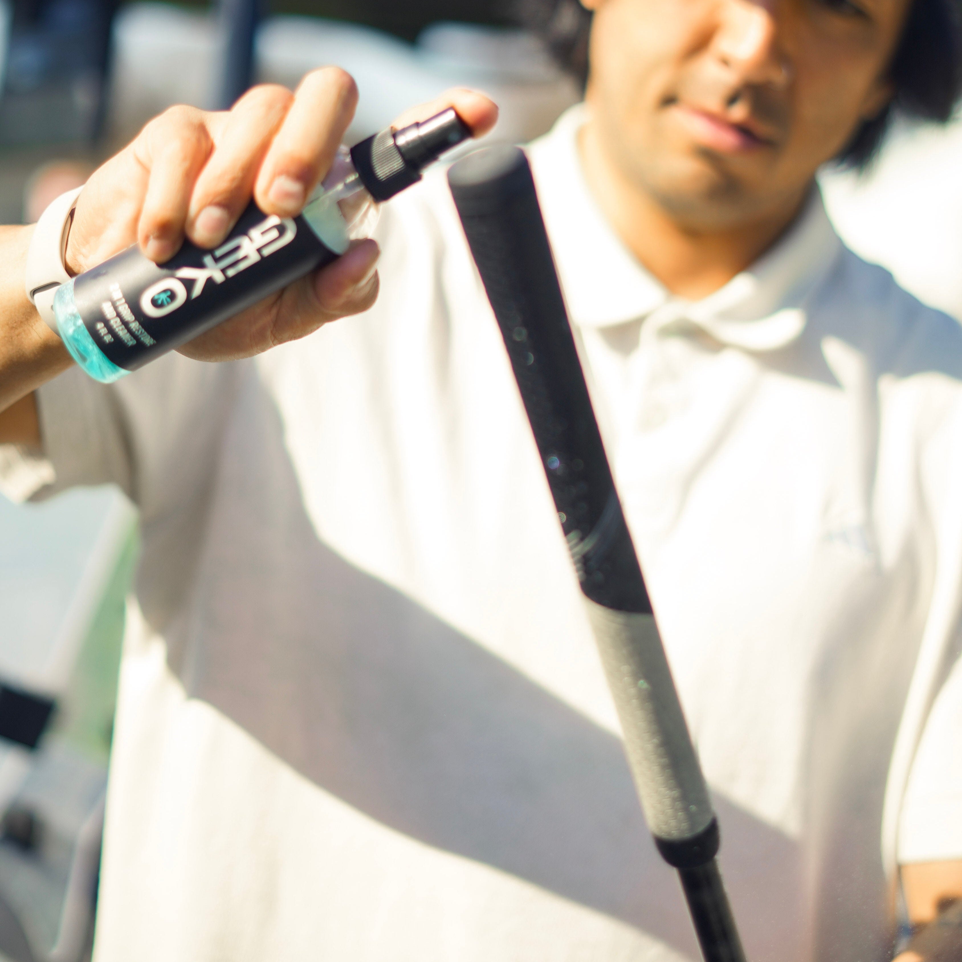 Person on a golf course holding a golf club and a geko bottle, with a blurred background.
