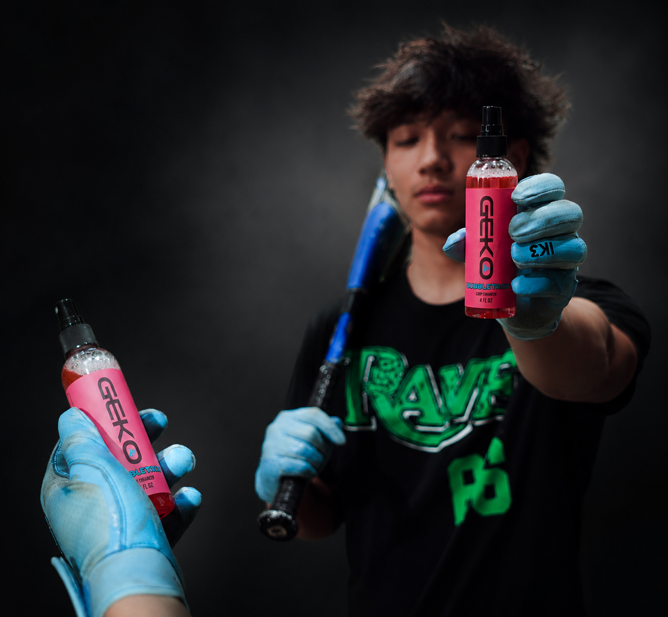A person in a black graphic T-shirt holds up two pink spray bottles labeled 'RAVE' while wearing blue gloves, with a blurred dark background.